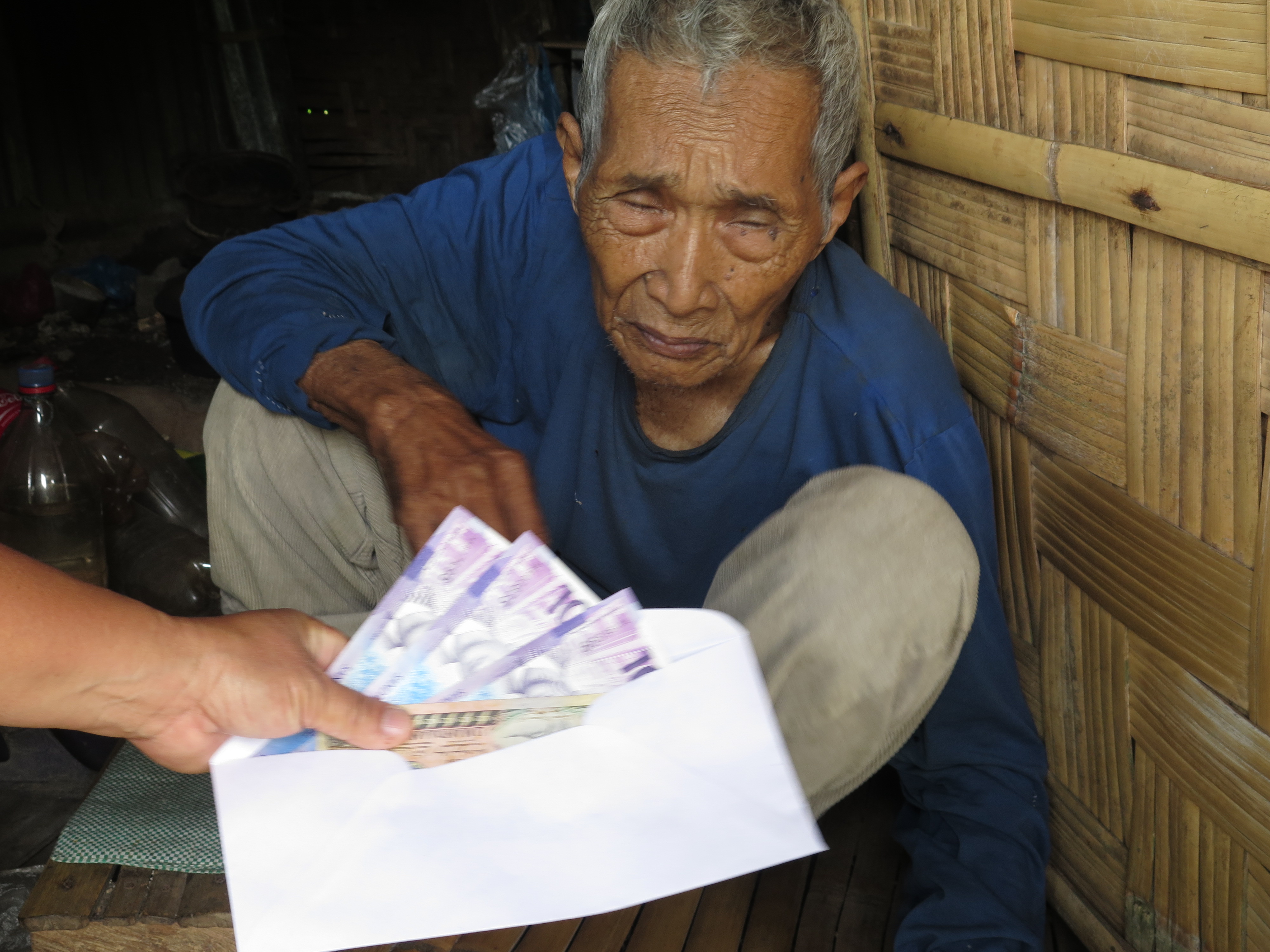 Photo is an image of an elderly man being given cash from his limited social pension.