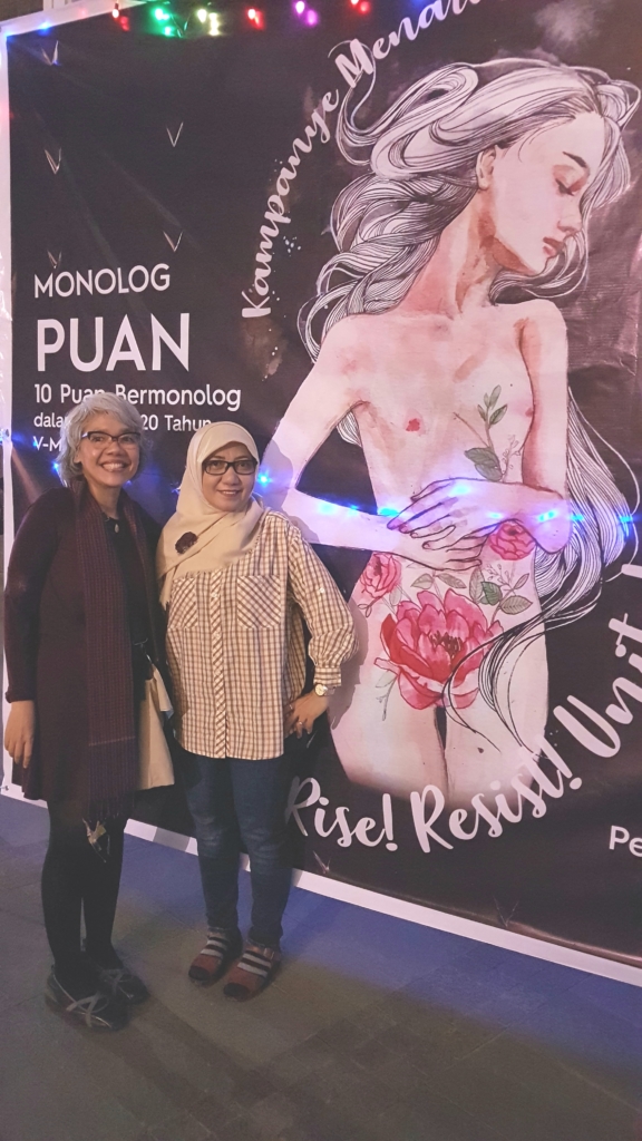 Image of Dewi S. Tjakrawinata standing in front of the One Billion Rising 2018 Event poster.